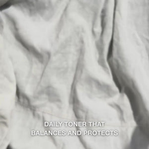 Close-up of a hand gently pressing a few drops of clear, water-like Face Tonic infused with Tea Tree Oil onto a cotton pad, then sweeping it softly across clean facial skin: the light, refreshing fluid soothes, deep-cleanses, hydrates, and leaves skin feeling renewed and lightly prepped for moisturizer.